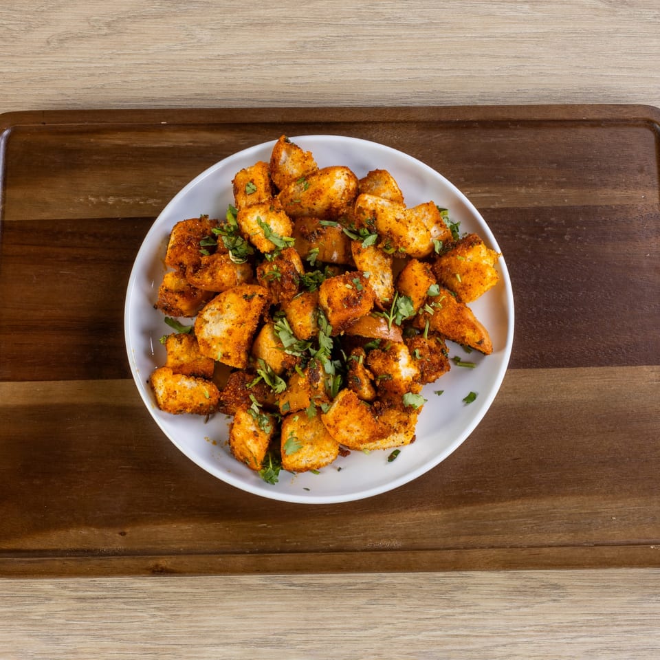 A white plate filled with golden-brown Indian fried idli, garnished with fresh green cilantro.