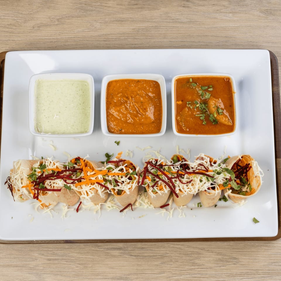 Indian dosa rolls topped with shredded cheese and vegetables, served with three dipping sauces.