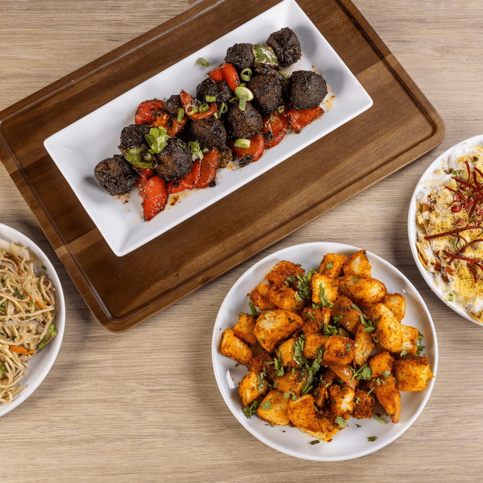 Overhead view of four Indian dishes: Manchurian, chili paneer, noodles, and dahi puri.