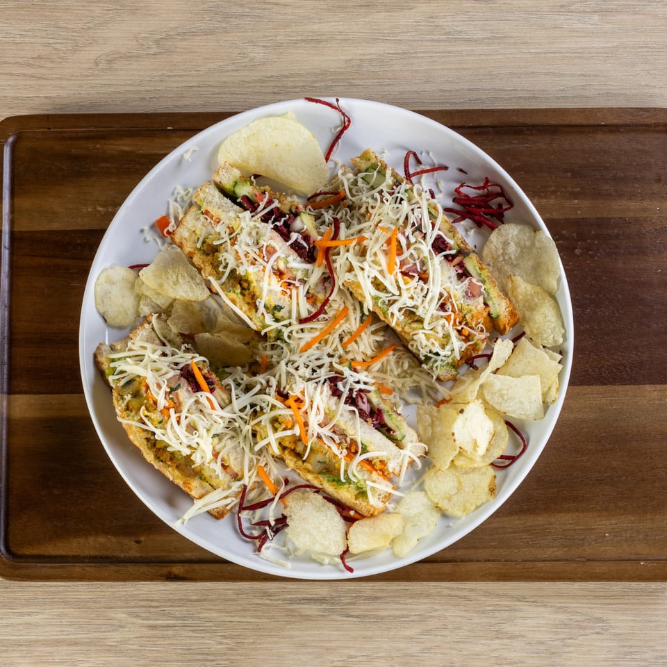Indian-style sandwiches topped with shredded cheese, carrots, and beets, served with potato chips.